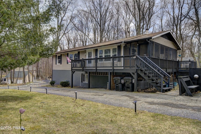 view of front of house with stairway, a sunroom, a wooden deck, and a front yard