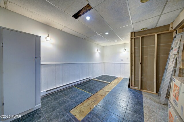 interior space featuring a drop ceiling, baseboards, wainscoting, a baseboard radiator, and recessed lighting