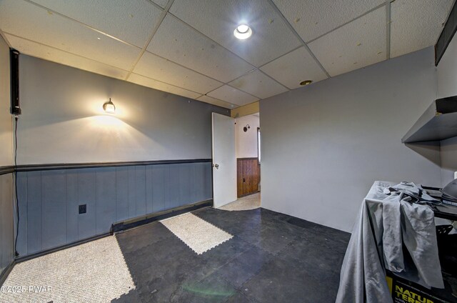 interior space with a drop ceiling and a wainscoted wall