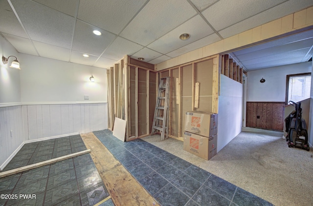 basement featuring recessed lighting, a wainscoted wall, and a drop ceiling