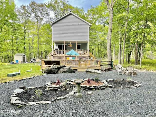 rear view of property with a lawn, a wooden deck, a storage unit, and an outdoor fire pit