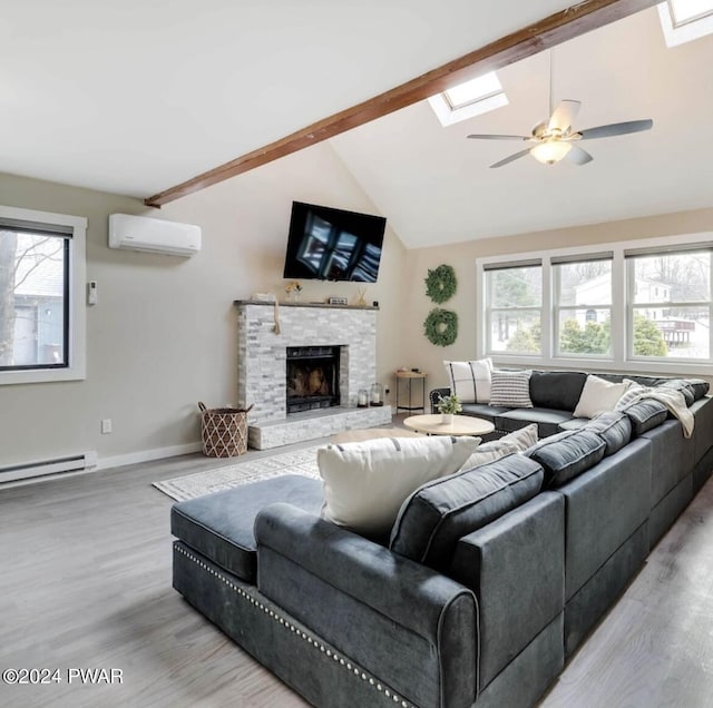 living room featuring a stone fireplace, light hardwood / wood-style flooring, vaulted ceiling with skylight, ceiling fan, and a wall unit AC