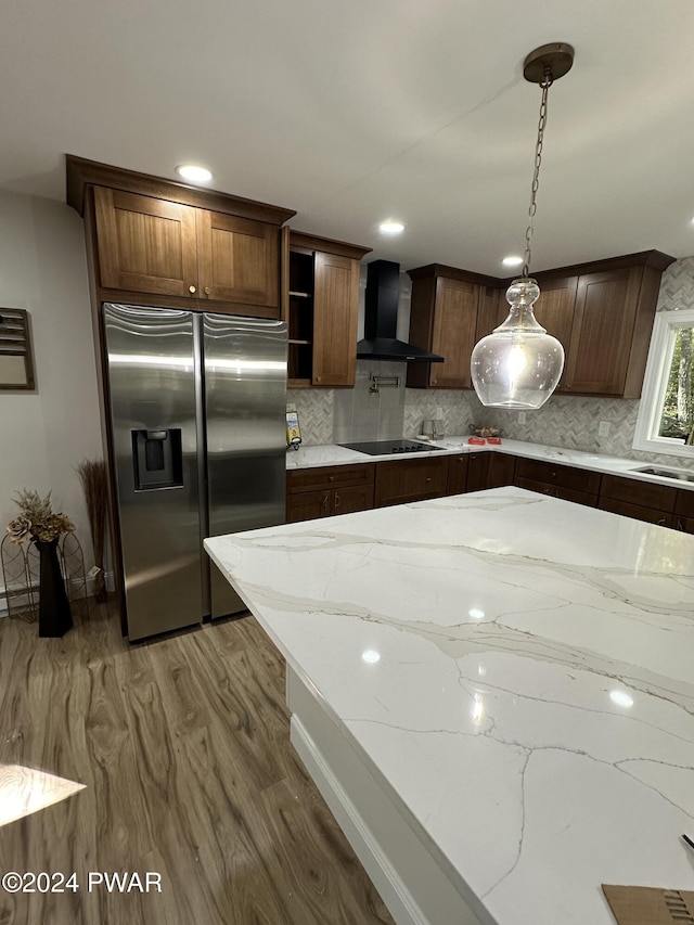 kitchen featuring black electric cooktop, light stone counters, wall chimney exhaust hood, and stainless steel refrigerator with ice dispenser