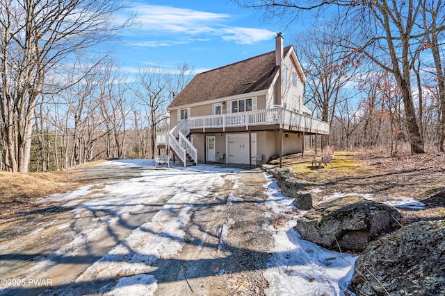 back of house with a deck, aphalt driveway, stairway, a shingled roof, and a chimney