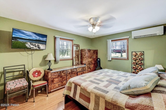 bedroom with a wall mounted AC, ceiling fan, and light hardwood / wood-style flooring