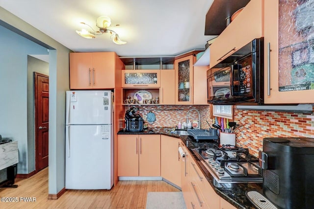 kitchen with sink, dark stone countertops, white refrigerator, light hardwood / wood-style floors, and stainless steel gas cooktop