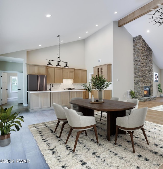 dining space featuring a stone fireplace, light hardwood / wood-style flooring, high vaulted ceiling, and beamed ceiling