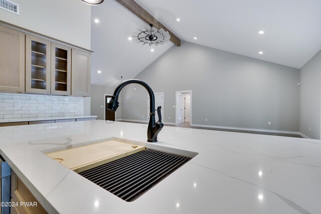 room details featuring light brown cabinets, backsplash, sink, light stone countertops, and beamed ceiling