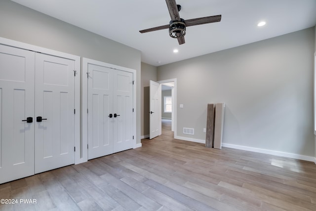 unfurnished bedroom with ceiling fan, two closets, and light wood-type flooring