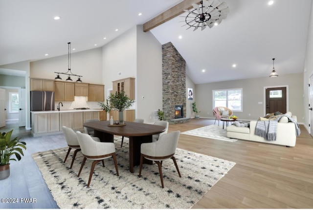 dining space with high vaulted ceiling, a stone fireplace, sink, light wood-type flooring, and beam ceiling