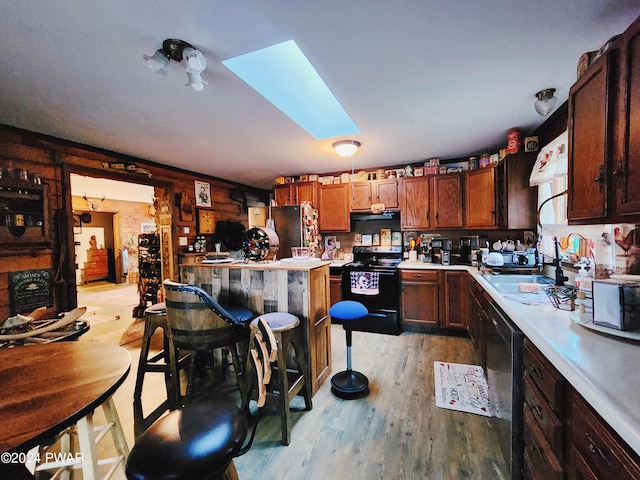 kitchen featuring a kitchen breakfast bar, light wood-type flooring, a skylight, sink, and black appliances