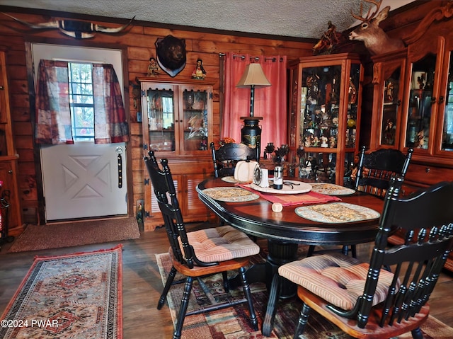 dining space with a textured ceiling, wooden walls, and dark hardwood / wood-style floors