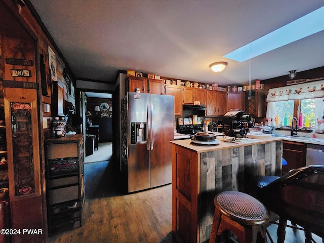 kitchen with hardwood / wood-style floors, sink, a skylight, a kitchen island, and stainless steel appliances