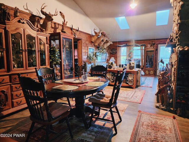 dining area featuring wooden walls, vaulted ceiling with skylight, and hardwood / wood-style floors