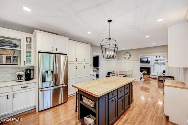 kitchen featuring appliances with stainless steel finishes, decorative light fixtures, white cabinets, butcher block countertops, and a kitchen island