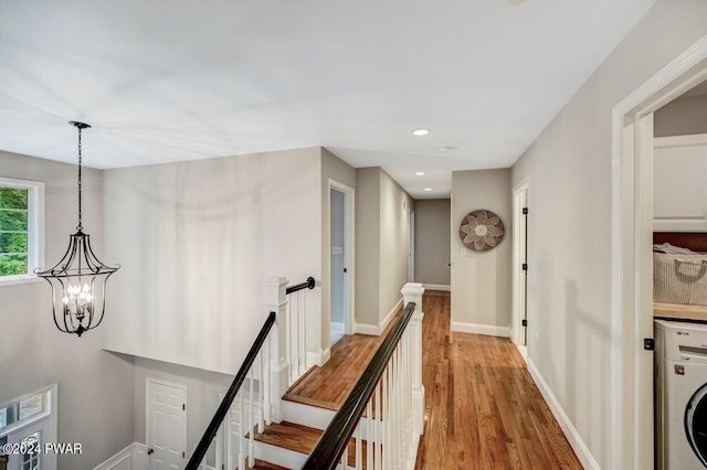 corridor with light hardwood / wood-style floors, washer / dryer, and an inviting chandelier