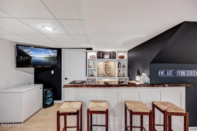 bar featuring a paneled ceiling, refrigerator, and light hardwood / wood-style floors