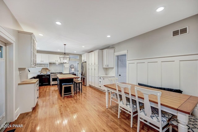 kitchen with white cabinetry, wooden counters, decorative light fixtures, a kitchen island, and appliances with stainless steel finishes