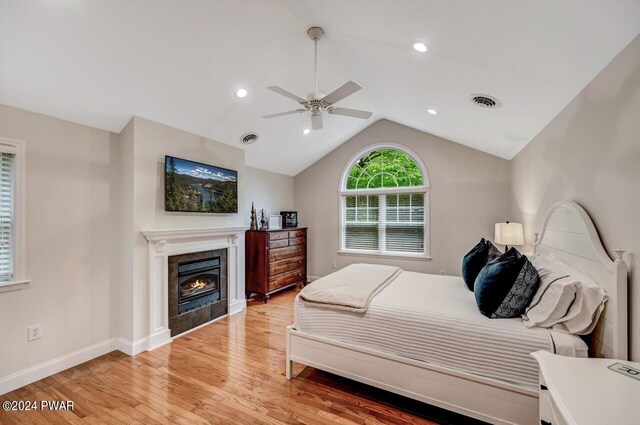 bedroom featuring light hardwood / wood-style flooring, vaulted ceiling, ceiling fan, and a tiled fireplace