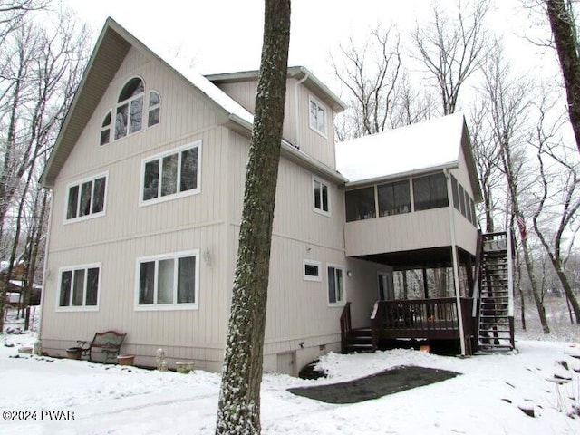 snow covered house featuring a sunroom and a deck