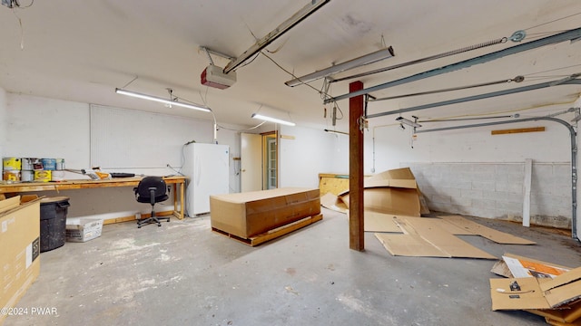 garage with white refrigerator, a garage door opener, and a workshop area