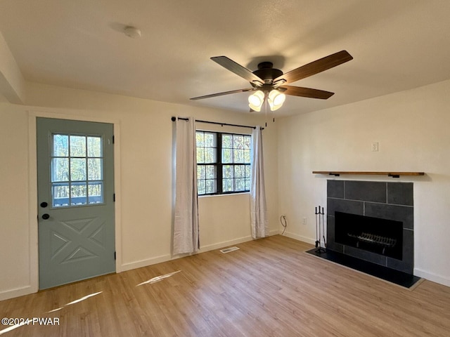 unfurnished living room featuring a tiled fireplace, ceiling fan, and light hardwood / wood-style flooring