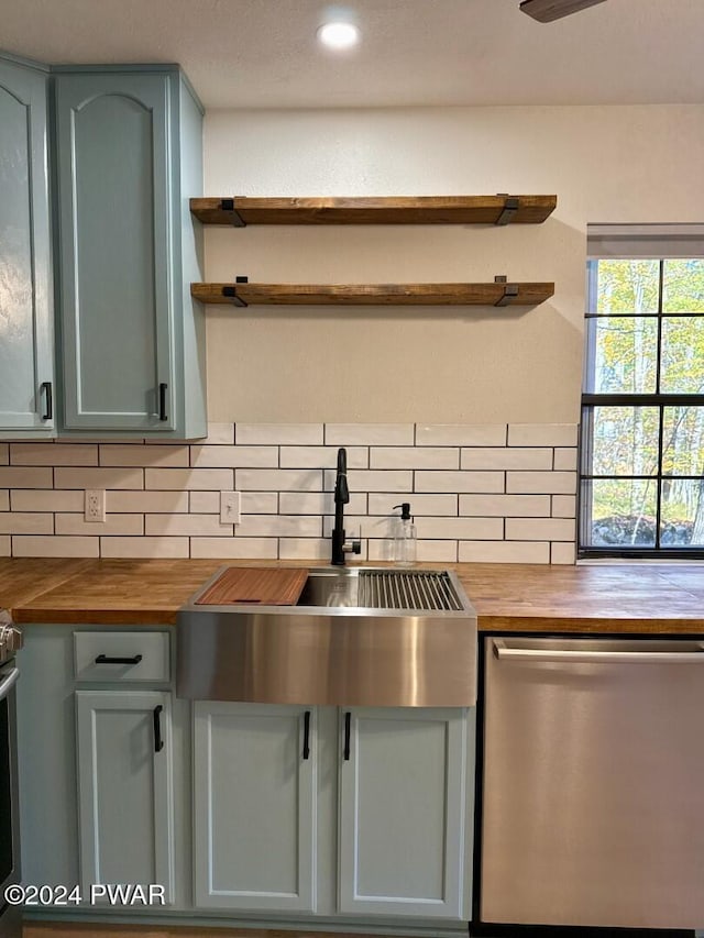 kitchen featuring butcher block countertops, decorative backsplash, stainless steel dishwasher, and sink