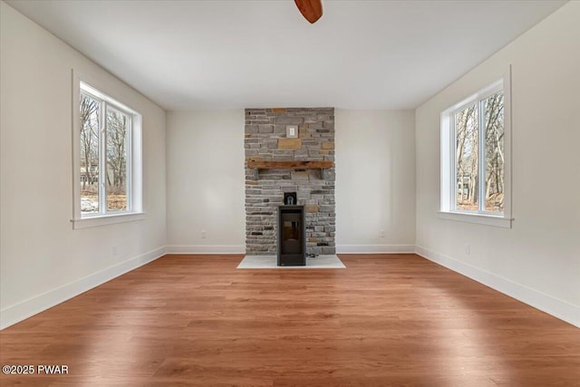 unfurnished living room featuring ceiling fan, a wood stove, a wealth of natural light, and light wood-type flooring