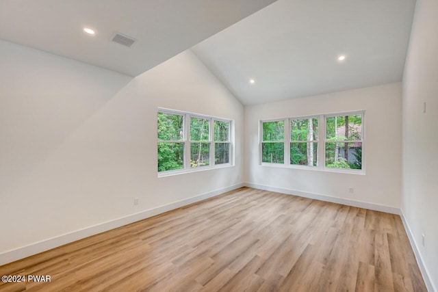 empty room featuring a healthy amount of sunlight, light wood-type flooring, and vaulted ceiling