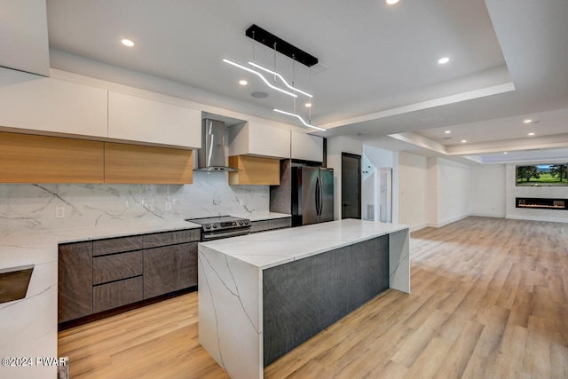 kitchen with light stone countertops, appliances with stainless steel finishes, wall chimney exhaust hood, white cabinetry, and hanging light fixtures