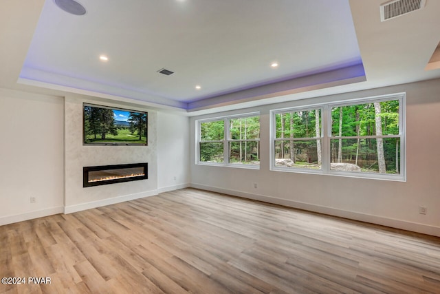 unfurnished living room with a tray ceiling and light wood-type flooring