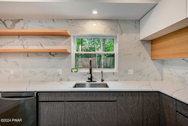 kitchen with stainless steel dishwasher, backsplash, light stone countertops, and sink