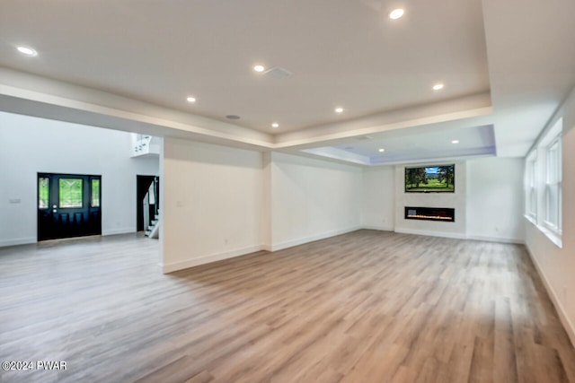 unfurnished living room with a raised ceiling and light wood-type flooring