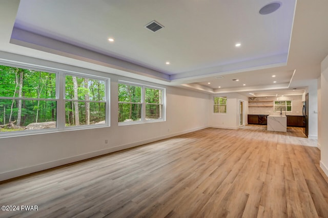 unfurnished living room with a tray ceiling, light hardwood / wood-style flooring, and sink