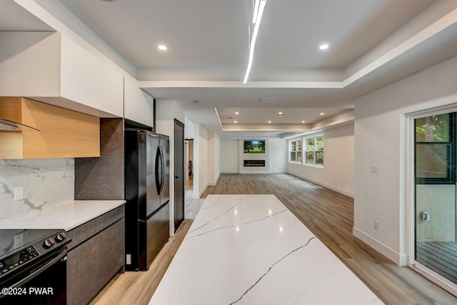 kitchen with black appliances, white cabinets, a raised ceiling, tasteful backsplash, and light stone counters