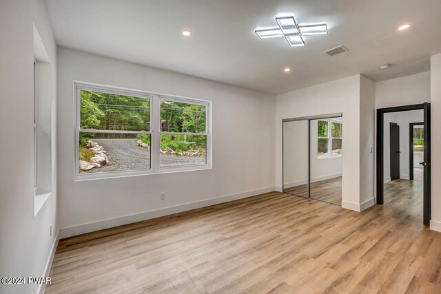 unfurnished bedroom featuring multiple windows, light hardwood / wood-style floors, and a closet