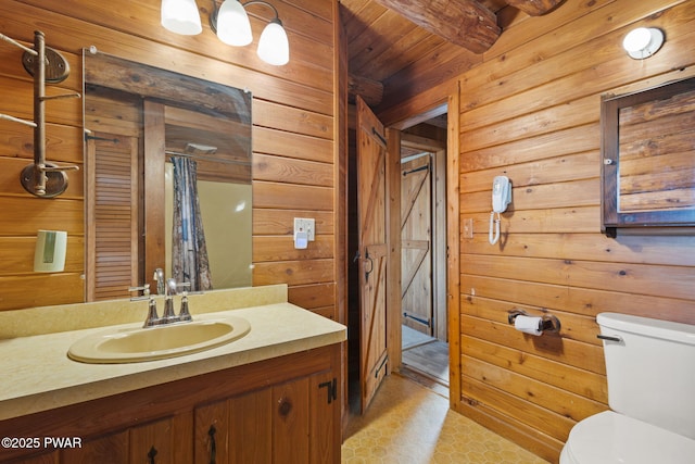 bathroom featuring vanity, wooden walls, wooden ceiling, beamed ceiling, and toilet