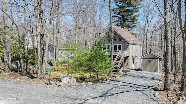 rustic home with driveway, a deck, an outbuilding, a carport, and stairs