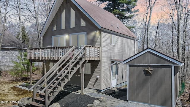 rear view of property featuring a wooden deck, roof with shingles, a storage unit, an outbuilding, and stairway