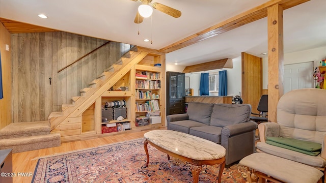 living room featuring stairs, wood finished floors, lofted ceiling with beams, wooden walls, and a ceiling fan