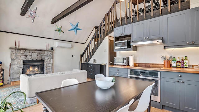 kitchen with lofted ceiling with beams, an AC wall unit, wooden counters, stainless steel appliances, and under cabinet range hood
