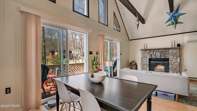 dining space with a healthy amount of sunlight, a high ceiling, a stone fireplace, and wood finished floors