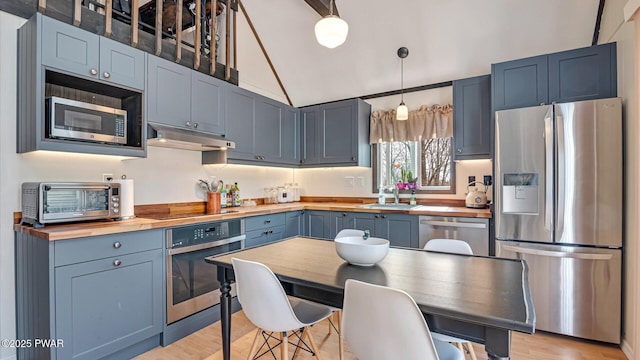 kitchen with butcher block countertops, a sink, under cabinet range hood, and stainless steel appliances