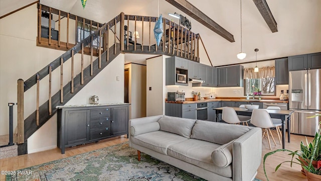 living area with light wood finished floors, beam ceiling, high vaulted ceiling, and stairway