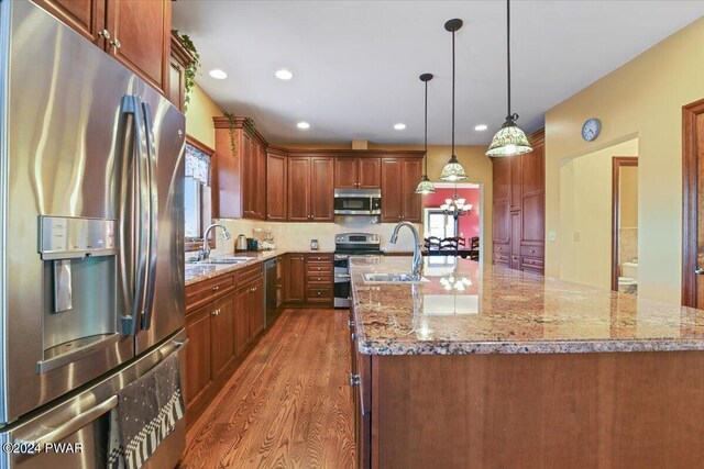 1075 Owego Tpke, Honesdale, PA 18431 - kitchen featuring appliances with stainless steel finishes, wood finished floors, light stone counters, a center island with sink, and decorative light fixtures