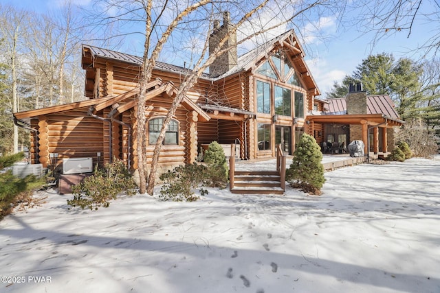 view of front of home with a chimney, a standing seam roof, metal roof, log exterior, and a wooden deck