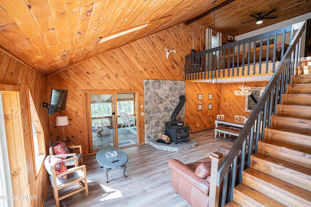 unfurnished living room featuring wooden ceiling, lofted ceiling, a wood stove, ceiling fan with notable chandelier, and light wood-type flooring