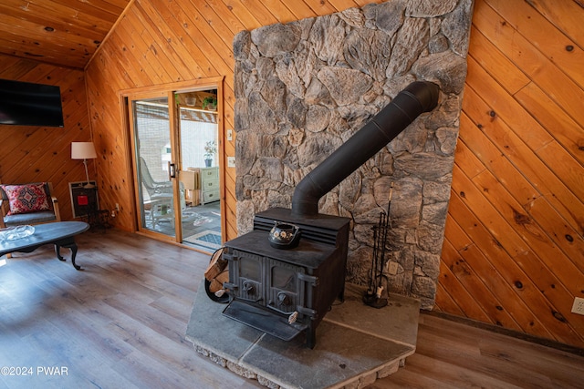 living room with a wood stove, wood-type flooring, vaulted ceiling, wooden walls, and wood ceiling