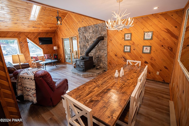 dining area featuring a chandelier, dark hardwood / wood-style flooring, a wood stove, and lofted ceiling with skylight