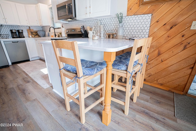 kitchen featuring decorative backsplash, appliances with stainless steel finishes, a kitchen breakfast bar, light hardwood / wood-style flooring, and white cabinetry